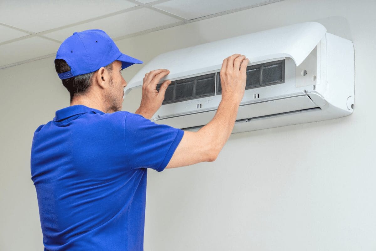 a professional HVAC technician in blue shirt and baseball cap inspecting a ductless mini split wall unit