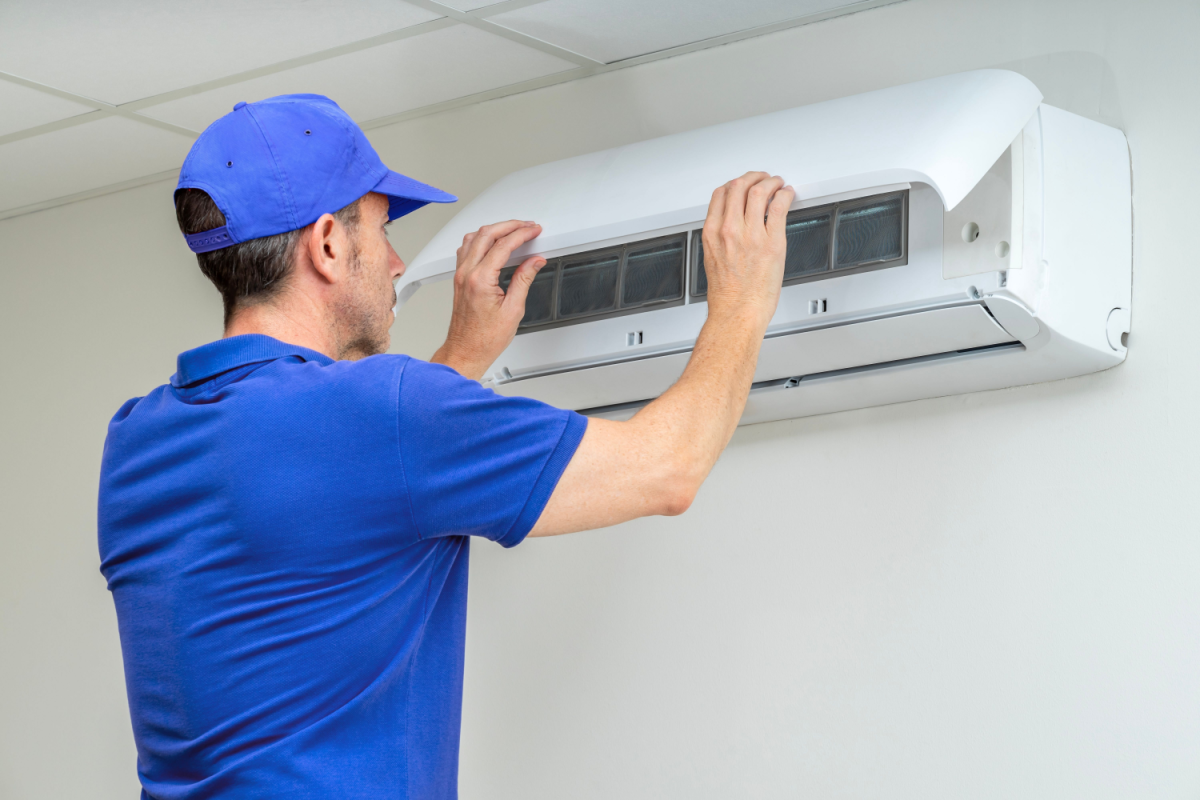 a professional HVAC technician in blue shirt and baseball cap inspecting a ductless mini split wall unit